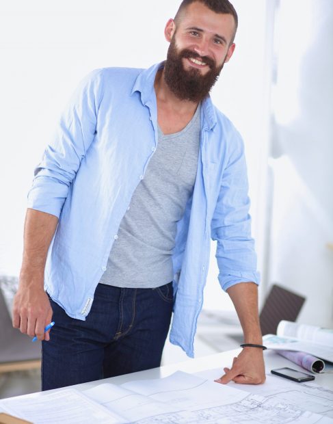 Portrait of male designer with blueprints at desk in office.